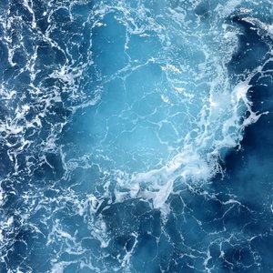 High angle shot of swirling turquoise ocean waves creating a dynamic seascape pattern.