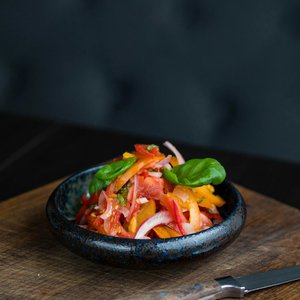 Fresh vegetable salad with colorful peppers and onions in a black bowl on a wooden board.