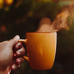 Hand holding a steaming orange mug outdoors in warm morning sunlight, creating a cozy atmosphere.