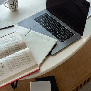 A cozy indoor workspace featuring a laptop, open book, notepad, and coffee, perfect for studying or remote work.