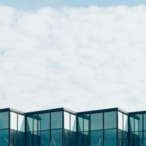 Low angle view of a modern glass building with a cloudy sky background, showcasing contemporary architecture.
