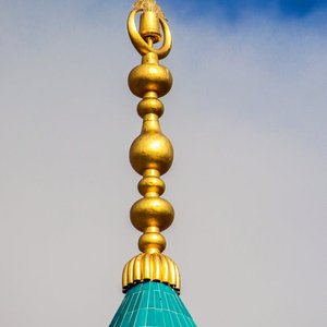 Stunning photo of a golden rooftop finial standing against a clear blue sky, showcasing geometric patterns.
