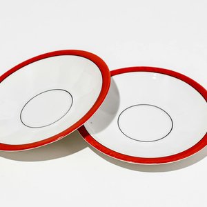 Two minimalist white porcelain plates with red trim on a white background.