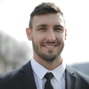 A smiling businessman in a suit standing outdoors with a bright expression.