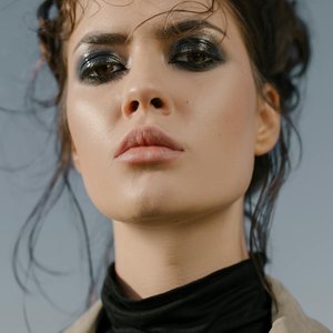 Close-up portrait of a woman with intense eye makeup and strong facial expression outdoors.