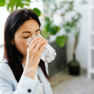 Adult woman sipping water from a glass in a modern office setting.