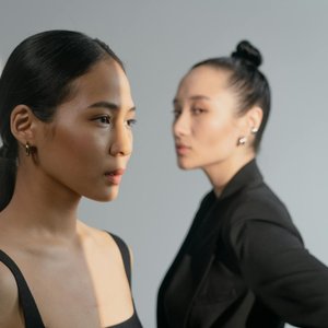 A fashionable portrait of two women in black attire, with one in focus and the other blurred, set against a light background.