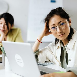 Focused woman with eyeglasses working on a laptop in an office setting.