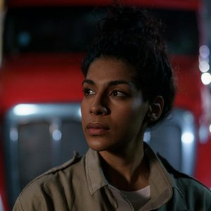 Woman in uniform looking away thoughtfully in front of a truck at night.