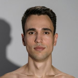 Portrait of a young adult man with a neutral expression in a studio setting. Soft lighting and minimal background.