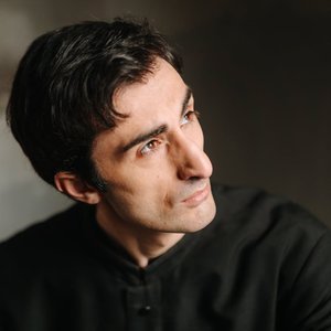 A thoughtful portrait of a young man with dark hair looking sideways, in a dimly lit room.