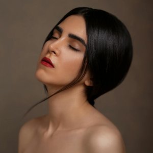 Close-up studio portrait of a serene woman with red lips and dark hair, eyes closed, ambient lighting.
