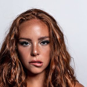 Studio headshot of a young woman with curly red hair on a white background.