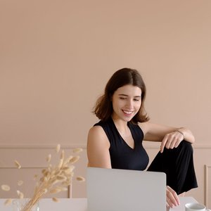 A cheerful woman works on her laptop at home, enjoying a relaxed lifestyle.
