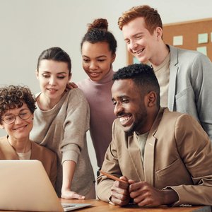 A group of diverse young professionals happily collaborating around a laptop indoors.