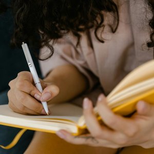 Person writing in a yellow notebook indoors, focusing on ideas.