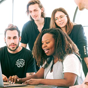 A diverse group of young professionals collaborating around a laptop in a modern office setting. Perfect for business or tech concepts.