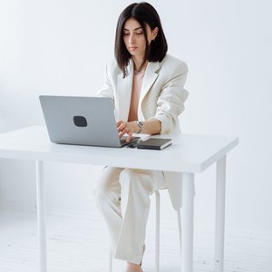 Businesswoman in a white suit working on a laptop in a minimalist office setting.