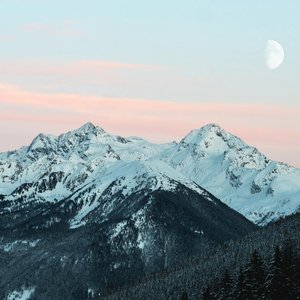 Majestic snow-covered mountain range with a rising moon and pink sunset sky.