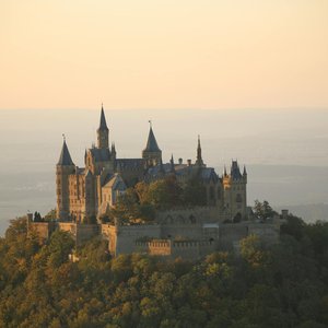 A captivating aerial shot of Hohenzollern Castle bathed in sunset light, surrounded by lush forests.