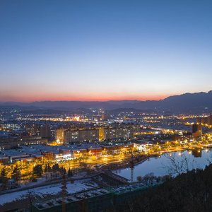 Stunning twilight cityscape with vibrant lights and mountain backdrop.