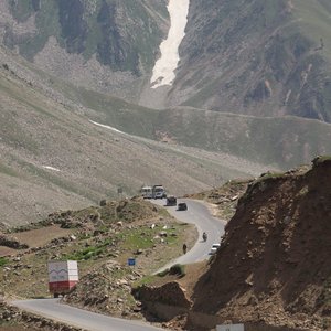 Winding mountain road with cars overlooking scenic snow-capped peaks on a sunny day.