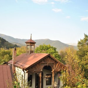 A picturesque mountain cottage surrounded by lush foliage under a bright sky.
