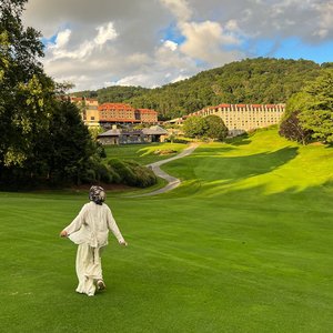 Woman in white walking on lush green lawn at a resort in North Carolina, USA during a sunny day.