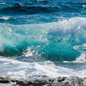 Dynamic ocean waves splashing against rocky shore, capturing sea foam and deep blue hues.