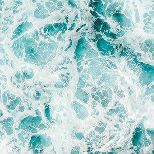 Aerial view of vibrant ocean waves and frothy seafoam creating abstract patterns.