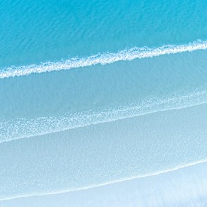 Aerial view of bright blue sea with foamy waves near sandy beach in daylight