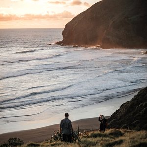 Tranquil New Zealand beach scene at sunset with two people enjoying the view.