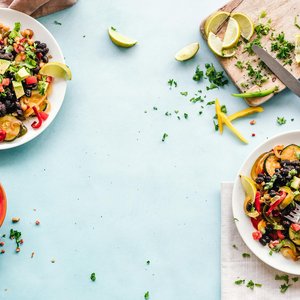 Colorful Mexican salad with avocado, black beans, and lime on a light blue surface.