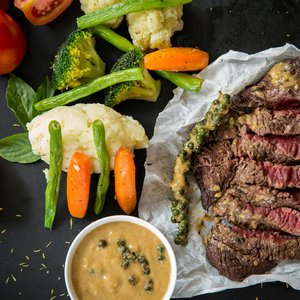 Grilled steak served with fresh vegetables and pepper sauce, presenting a colorful and appetizing meal.