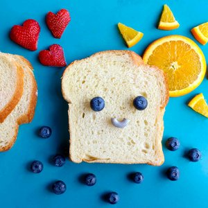 Fun and colorful toast face art with blueberries, strawberries, and orange slices on a blue background.