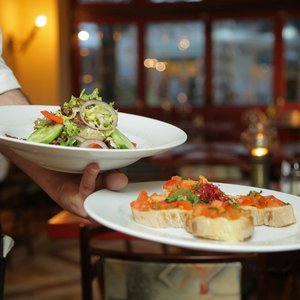 A waiter serves a fresh salad and hors d'oeuvres in a cozy restaurant setting.
