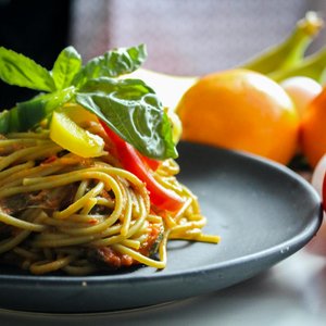 A plate of spaghetti garnished with basil and fresh vegetables, showcasing Italian cuisine.