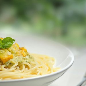 Close-up of freshly made spaghetti topped with basil and creamy pesto sauce in a white dish.