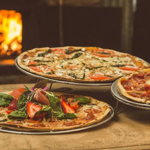Trio of gourmet pizzas with unique toppings near a wood-fired oven, ideal for food enthusiasts.