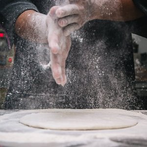 A chef clapping hands over dough, releasing flour in a kitchen setting.