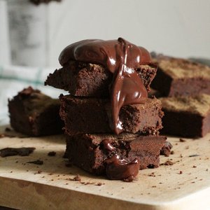 Delicious stack of chocolate brownies drizzled with gooey syrup on a wooden board.