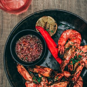 Close-up of spicy grilled shrimp with dipping sauce and grilled lime slice on a plate.