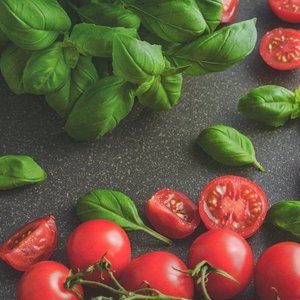Organic basil leaves with ripe tomatoes on a rustic countertop, highlighting fresh ingredients for cooking.