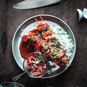 Delicious grilled skewers with rice and salsa served on a wooden table.