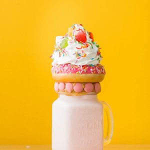 Vibrant milkshake adorned with a donut, whipped cream, and candy against a yellow background.