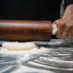 Close-up of a chef rolling dough with a wooden pin, capturing the art of baking.