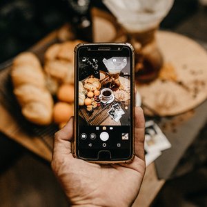 Warm indoor scene with smartphone capturing coffee and pastries on table.