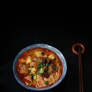 Close-up of a flavorful beef ramen noodle dish with chopsticks on a dark background.