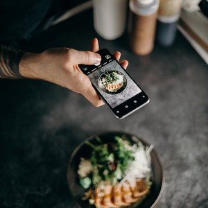 A person photographing a beautifully plated Asian dish with a smartphone camera.
