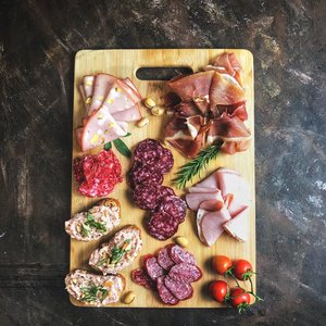 Delicious selection of cold cuts and bread on a wooden board with fresh herbs and tomatoes.